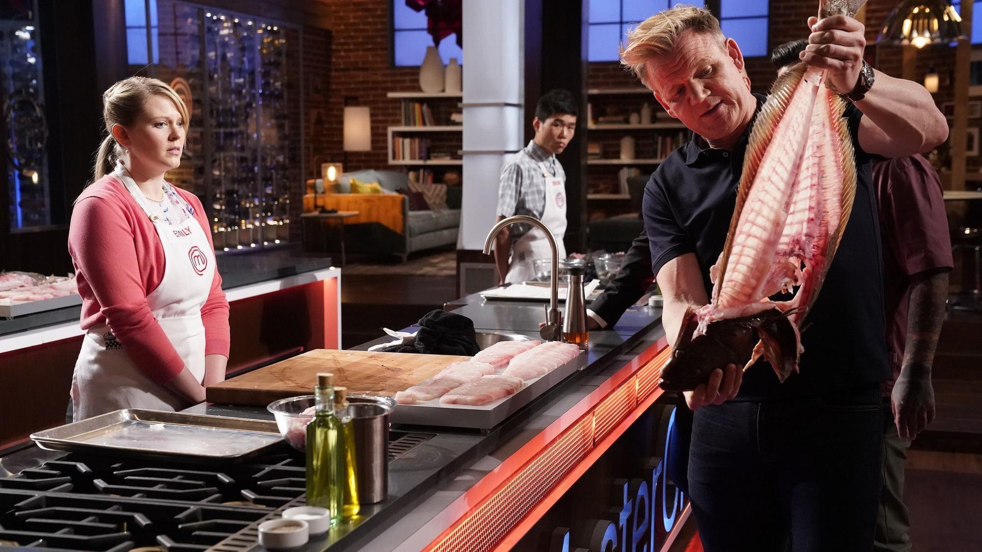 An image from Masterchef USA. Gordon Ramsay is holding the carcass of a fish. A contestant observes... horrified? At least intimidated.